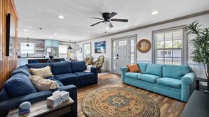 A spacious living area with a large blue sofa, a smaller blue sofa, a wooden coffee table, and a patterned rug.