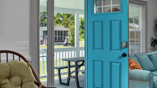A room with a teal door, a wooden chair, a sofa, and a view of a porch with a table and chairs.