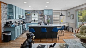 A modern kitchen with blue cabinets, a central island with bar stools, and a dining area with a bench.