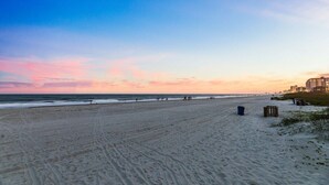 A wide sandy beach with footprints, a few scattered trash bins, and a distant building.