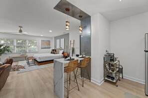 A modern living space with a bed, seating area, dining table, and kitchen area.