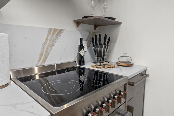 A kitchen with a built-in stovetop, knife block, wine glasses, and a glass container on the counter.