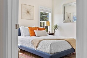 Un dormitorio con cama, almohadas, una ventana y un espejo.