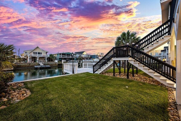 A waterfront property with a pool, a grassy lawn, and a staircase leading to a deck.