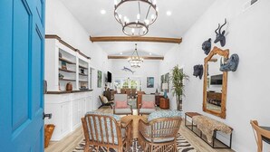 A room with a dining table, chairs, a zebra-patterned rug, a chandelier, and a mirror with animal heads. - Hem's Hideout | 5BR Tropical Oasis w/ Heated Pool (North Myrtle Beach)