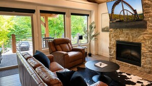 Una sala de estar moderna con sofás de cuero, una chimenea, una pared de piedra y un televisor montado en la parte superior.