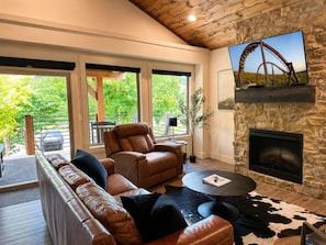 A modern living room with leather sofas, a fireplace, a stone wall, and a TV mounted above it.