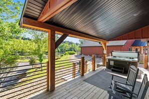 A covered outdoor deck with a hot tub, wooden chairs, and a view of a green landscape. - Lakefront, Amazing LakeView, Private Hot Tub! (Hollister)