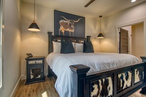 A bedroom with a large bed, dark wood headboard, two bedside tables, a mounted artwork of a bull, and pendant lighting. - Lakefront, Amazing LakeView, Private Hot Tub! (Hollister)