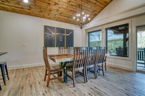 A dining area with a wooden table and chairs, a chandelier, and large windows with a view of the outdoors. - Lakefront, Amazing LakeView, Private Hot Tub! (Hollister)