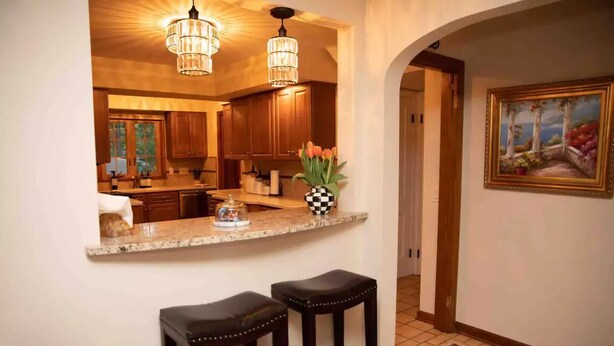 A kitchen with wooden cabinets, a marble countertop, and two black barstools.