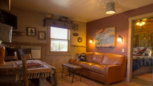 A cozy living room with a leather sofa, wooden dining table, and a window with blinds. - Utah's Best-Kept Secret: Secluded and Serene Cabin Getaway, Uta's Best-Kept Secret: Secluded and Ser (Garfield County)