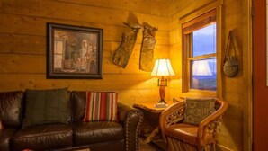 Una habitación acogedora con un sofá de cuero, un sillón de madera, una mesa con lámpara, un cuadro enmarcado y una ventana con vistas.