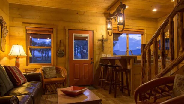 Interior acogedor de una cabaña con revestimiento de madera, un sofá, una mesa de comedor y una zona de bar.