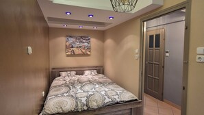 Une chambre à coucher avec un lit, un luminaire au plafond, une porte et un tableau accroché au mur.