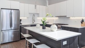 A modern kitchen with white cabinets, a stainless steel refrigerator, a central island with bar stools, and pendant lighting. - 2 Newly Built Luxury Condos with Private Roofdeck! (Chicago)
