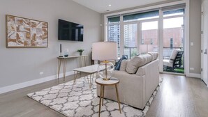 A modern living room with a sofa, a coffee table, a TV, and a large window. - 2 Newly Built Luxury Condos with Private Roofdeck! (Chicago)