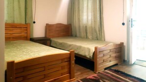 A bedroom with two wooden beds, a nightstand, and a window with curtains. - Lileo (Akhmeta)