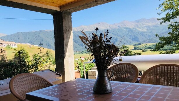 A patio with a table and chairs, a vase with dried plants, and a view of mountains. - Lileo (Akhmeta)