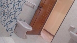 A bathroom with a bidet, a wooden door, and a patterned wall. - Cubico Tota (Praia)