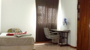 A small, narrow room with a bed, a desk, and a chair. - Cubico Tota (Praia)