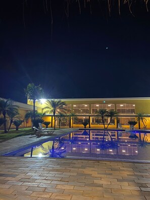 A nighttime view of a hotel with a swimming pool, palm trees, and a well-lit building facade. - Cerrado Plaza Hotel (Ribas do Rio Pardo)