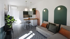 Una cocina moderna con una isla central, un comedor con sillas y una sala de estar con sofá y cojines.