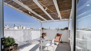 Terraza en la azotea con una mesa, sillas, una cesta de mimbre y vistas de la ciudad.