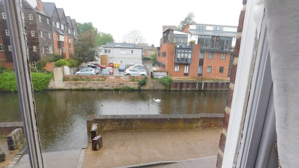 Blick aus einem Fenster auf einen Kanal mit einer Reihe geparkter Autos und Gebäuden im Hintergrund.