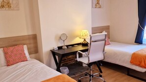 Ein Hotelzimmer mit zwei Betten, einem Schreibtisch mit Stuhl, einer Lampe und einem Wandspiegel.