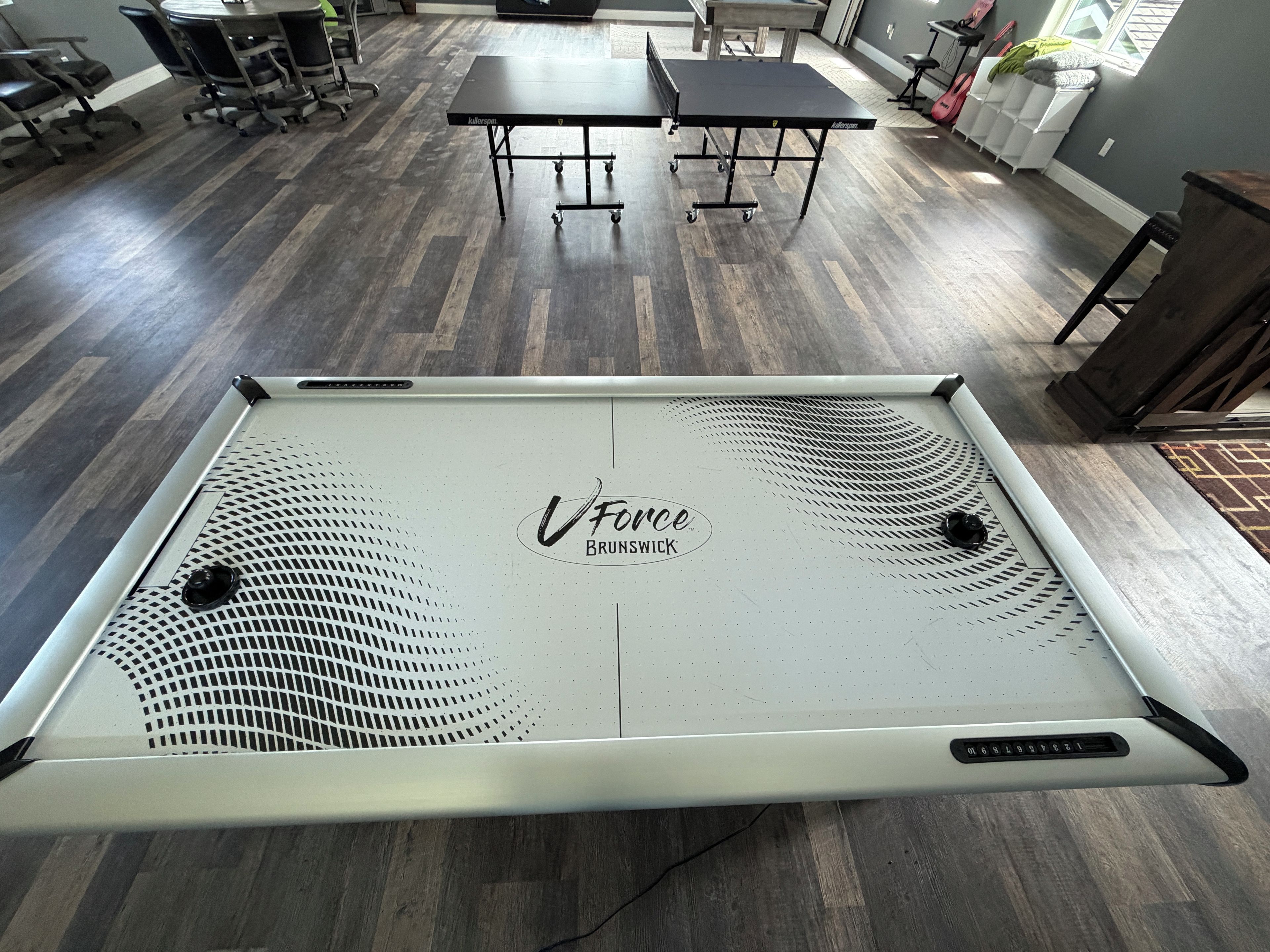 Une table de billard ornée du logo « Force Brunswick », dans une pièce dont le sol et les tables sont en bois.