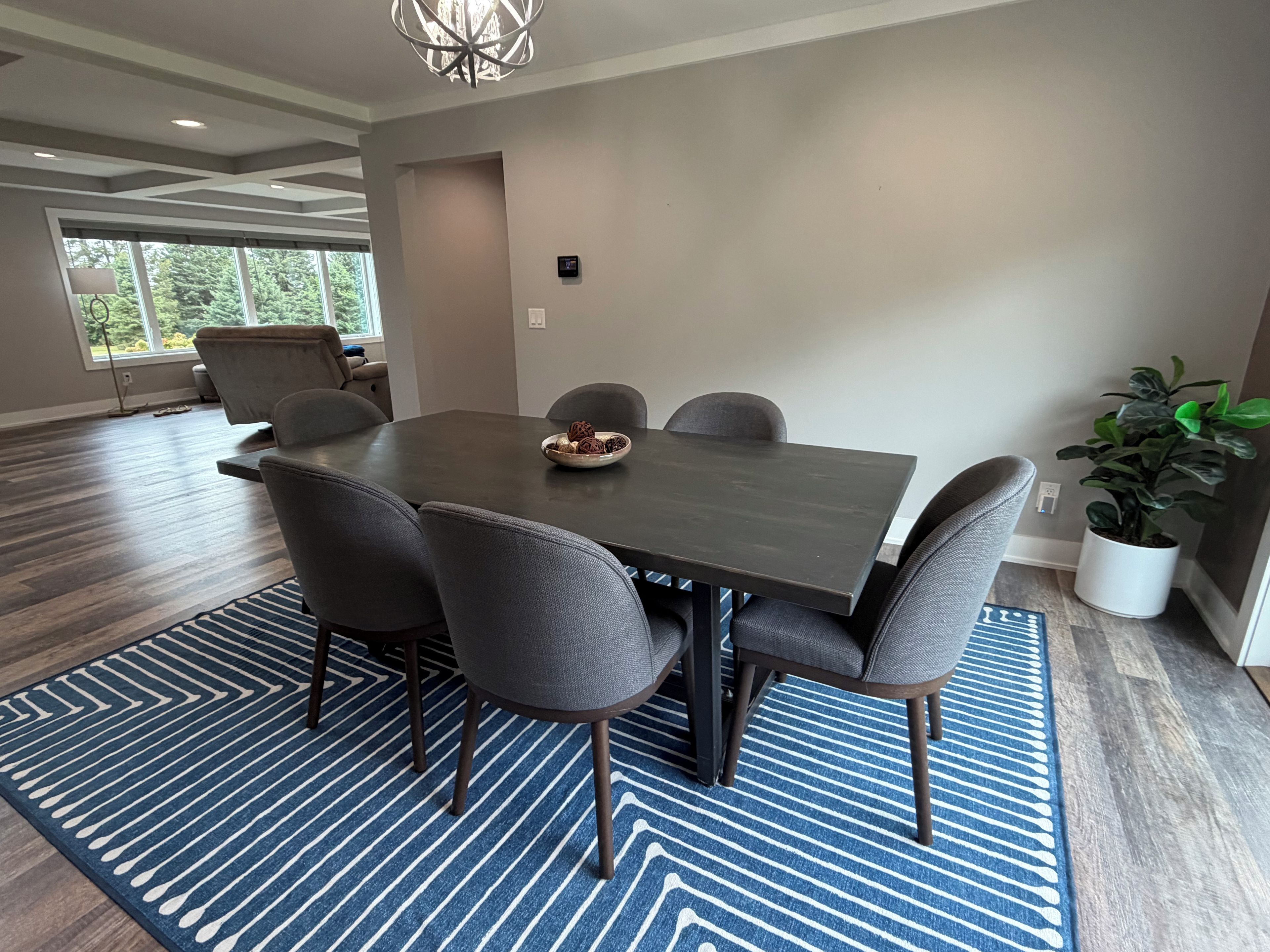 Un espace repas moderne avec une table rectangulaire entourée de six chaises, un tapis à motifs bleus et une plante en pot.