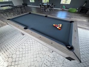A pool table with a set of balls in the center, surrounded by chairs and a table.