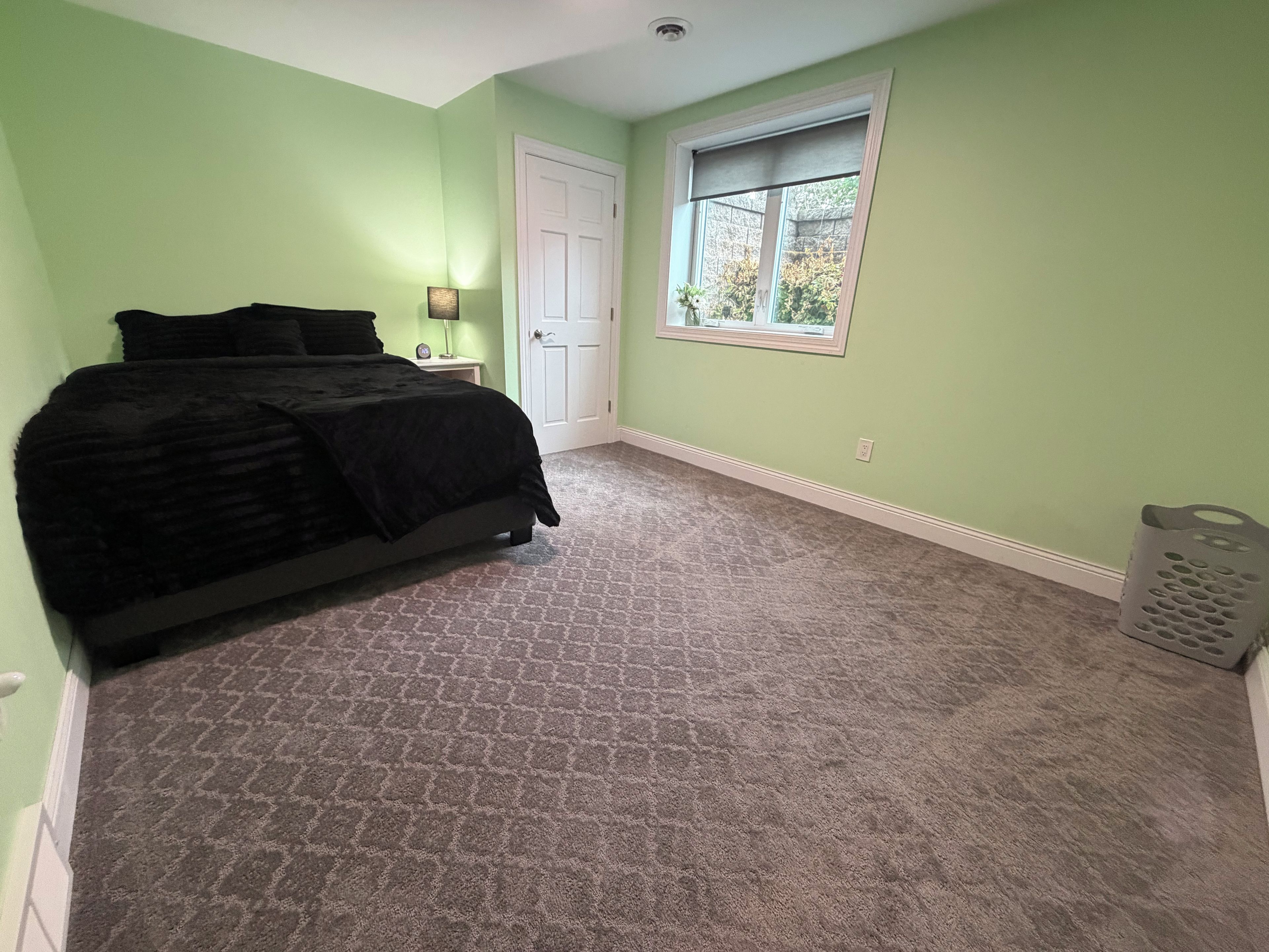Een slaapkamer met een bed, nachtkastje, raam en deur.