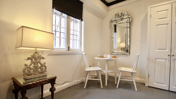 A room with a table and two chairs, a lamp, a mirror, and a door.