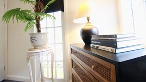 A room with a potted plant, a lamp, and a stack of books on a dresser.
