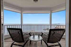 A covered outdoor seating area with two chairs and a table, overlooking a body of water and a distant island.