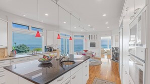 A modern kitchen with a large island, white cabinetry, and a view of the ocean. - Rockcleft (Marblehead)