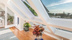 A modern loft bedroom with skylights, wooden flooring, and a city view.