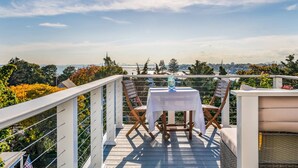 A balcony with a table and chairs, overlooking a scenic view of trees and a distant city skyline.