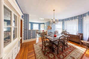 A dining room with a wooden table set for four, surrounded by chairs. There is a chandelier above the table and a patterned rug on the floor. - Belle Femme (Salem)