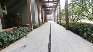 A covered walkway with a drainage grate, bordered by greenery and a brick wall. - Lian'Jia Apartment Hotel (Shenzhen Dachong Xincheng Huayuan) (Shenzhen)