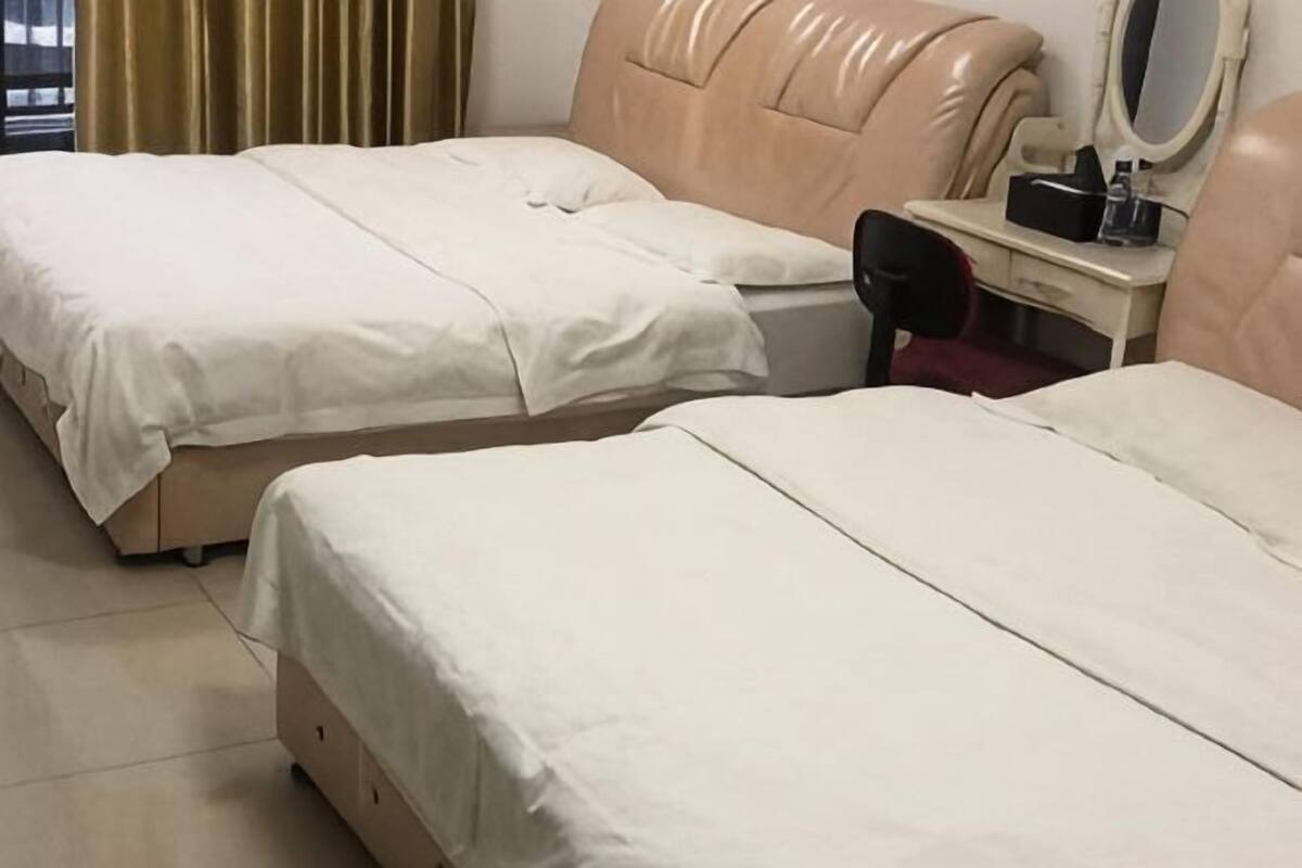 Two beds with beige headboards, a desk with a mirror, and a chair.