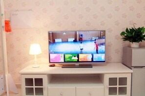 A television on a white cabinet with a floral wallpaper background. - Lian'Jia Apartment Hotel (Shenzhen Dachong Xincheng Huayuan) (Shenzhen)