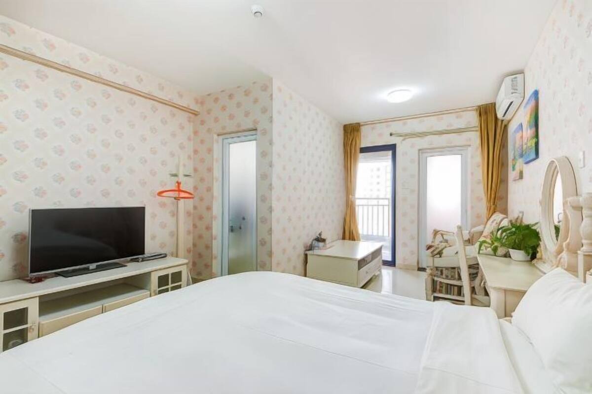 A hotel room with a bed, a desk, a television, a wardrobe, and a window with curtains.