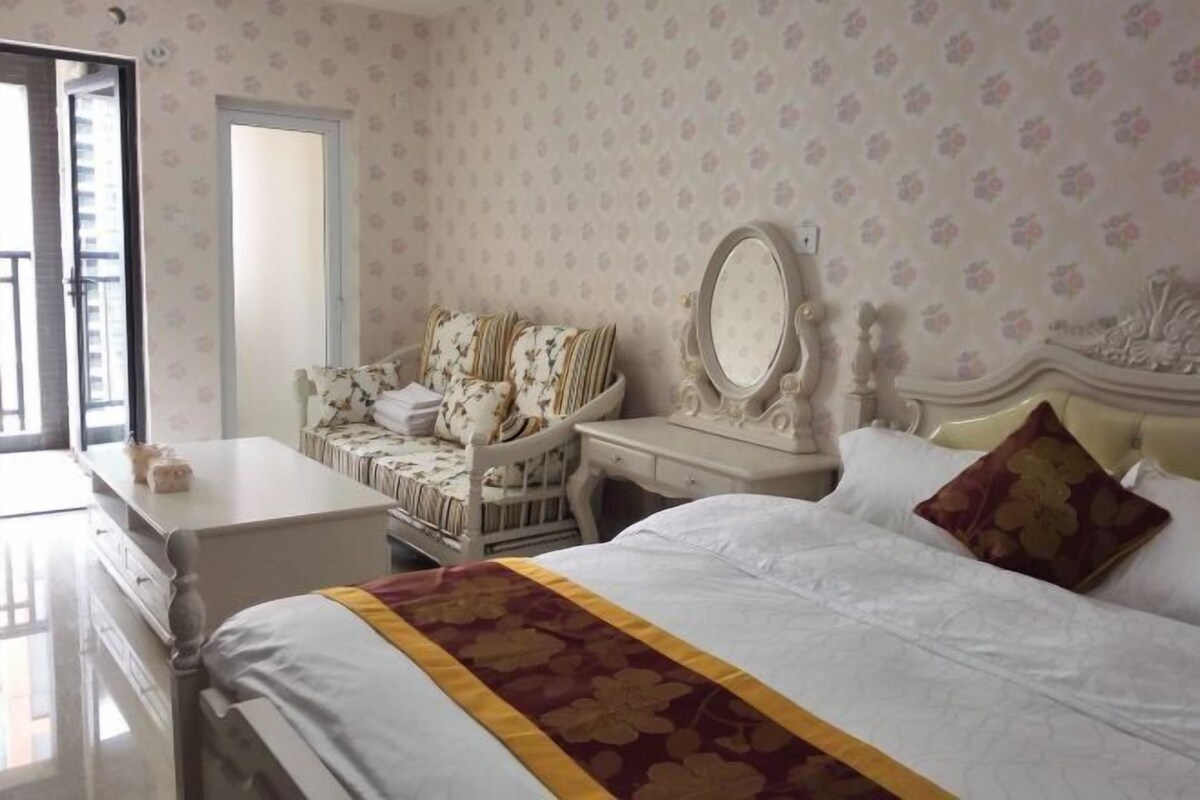 A bedroom with a bed, a vanity with a mirror, a chair, and a dresser.