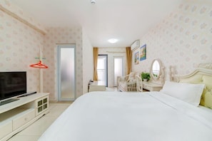 A bedroom with a bed, a TV, a dresser, a mirror, and a door.