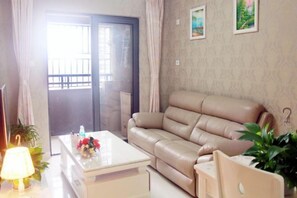 A living room with a beige leather sofa, a white coffee table with a floral arrangement, and a sliding glass door leading to a balcony. - Lian'Jia Apartment Hotel (Shenzhen Dachong Xincheng Huayuan) (Shenzhen)