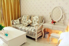 A room with a floral sofa, a white coffee table, a vanity with a mirror, and a small bench. - Lian'Jia Apartment Hotel (Shenzhen Dachong Xincheng Huayuan) (Shenzhen)