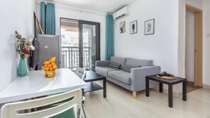 A modern living room with a grey sofa, a dining table with chairs, a small coffee table, and a kitchen area with a fridge and a sink. - Lian'Jia Apartment Hotel (Shenzhen Dachong Xincheng Huayuan) (Shenzhen)